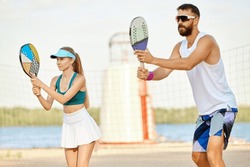 Team. Young man and woman playing paddle tennis on beach on warm summer day near river. Outdoor activity. Concept of sport, leisure time, active lifestyle, hobby, game, summertime, ad
