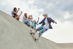 Friends, teengaers meeting at skate park for active leisure time. Boy in casucl clothes skateboarding on ramp. Concept of youth culture, sport, dynamic, extreme, hobby, action and motions, friendship