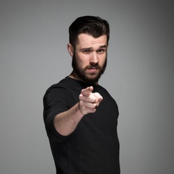 Young man with beard and mustaches, finger pointing towards the camera on a gray background
