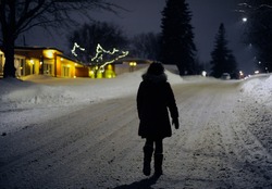 a lonely woman is walking in a snowy street on a winter evening