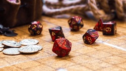 low angle shot featuring a collection of vibrant red RPG dice and golden gaming coins arranged on a battle map