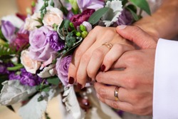 Newly married husband gently hold the arm of his wife with wedding bouquet on the background. 