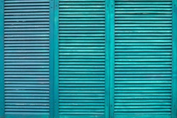 Green wooden shutters. Three wooden casement windows to block sunlight. Background with textured narrow boards of turquoise color. Old green wooden shutters tiled