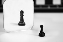 black chess pawn stands in front of the mirror, seeing reflection of queen. concept of career and personal growth, aspiration, improvement, self-confidence. pawn that would be king.