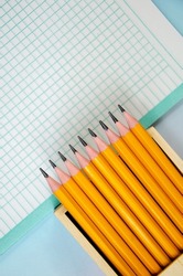 set of graphite pencils in an open wooden box and an empty blank on blue background. Pencils in pencil case and notebook sheet in cage. Banner, space for text. Back to School concept, top view