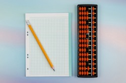 Notebook sheet in a cage, a pencil and an abacus for mental arithmetic on a colored background