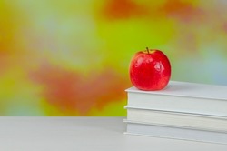 Stack of white books with juicy fresh apple on desktop over blurry autumn background. stacked books with red apple. Background for school design. Back to school.