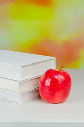 A juicy fresh apple stands on the desktop next to a stack of books over blurry autumn background. stacked books with apple. Background for school design. Back to school.