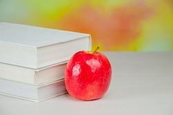 A juicy fresh apple stands on the desktop next to a stack of books over blurry autumn background. stacked books with apple. Background for school design. Back to school.
