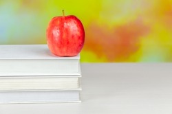 Stack of white books with juicy fresh apple on desktop over blurry autumn background. stacked books with red apple. Background for school design. Back to school.