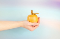 Wooden apple in an outstretched female hand on a blue background. Close-up, woman's hand holding an apple. Concept: temptation, knowledge, offer