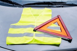 yellow reflective vest and warning triangle lie on hood of car. Safety on road in case of breakdown