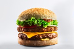 Double burger with cheese, tomato and lettuce on white table against white background.