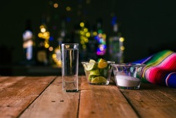 Shot of tequila served in a tequila glass on a wooden table. Blurred background. Rustic bar atmosphere.