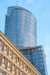 Two buildings from different eras: a modern glass skyscraper and an old low office building