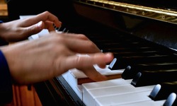 Child playing piano. Close up side view of blurred fast moving young hands and fingers playing a song on the keys of an upright shiny black piano.