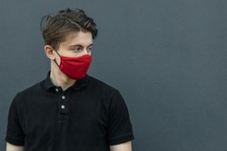 Close-up portrait of young man walking in black t-shirt and red medical mask on dark gray background for protect and stop viruses and coronavirus pandemic, covid-19 outbreak. Guy in red mask