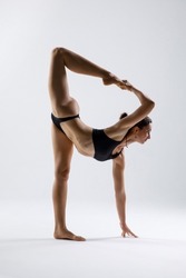 White beautiful european woman doing stretching. Woman in black sportswear. Gymnast. White studio background. Balance. Yoga pose. Sport. Practice