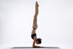 A woman in black stands on her hands. Gymnast. White beautiful European woman. White studio background. Balance. Yoga pose. Sport