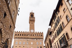 The famous Palazzo Vecchio in Florence, wide-angle shot, framed by houses from the Piazza Signoria on a cloudy day. Italian famous places
