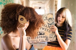 two young and beautiful women, one blonde and one African-American, doing the Ouija board in a corridor of an abandoned building. The women are invoking the spirits of the afterlife.
