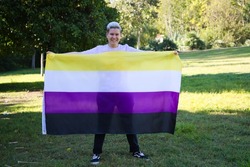 gender non-binary person holds the non-binary pride flag in his hands. He is looking at the camera. Concept of non-binary and androgynous. Diversity