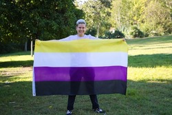 gender non-binary person holds the non-binary pride flag in his hands. He is looking at the camera. Concept of non-binary and androgynous. Diversity