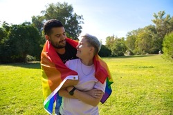 Non-binary gender person and gay man are embracing and carrying the gay pride flag on their backs. Concept of non-binary and androgynous. Diversity and gay pride.