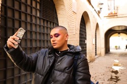 Non-binary and young person from South America is on holiday in Europe, the person is make up and wearing black clothes. He is visiting the city and takes pictures with his mobile phone. Travel.