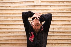 Portrait of a man dancing flamenco with a black shirt and red roses, on a brown background doing different postures with his hands. Feel passion. Flamenco dance concept cultural heritage of humanity.