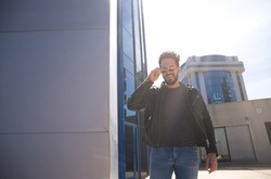 young and handsome man with beard, sculptural body and sunglasses is leaving the office where he works in a glass building. Concept management, administration, office, company, boss.
