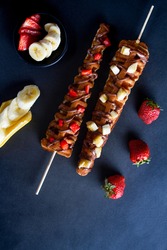 waffle sticks, 2 sticks glazed with chocolate and fruits, strawberries and bananas, black background 