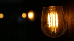 Very detailed macro of an Edison bulb with yellow light bokeh in the dark background.