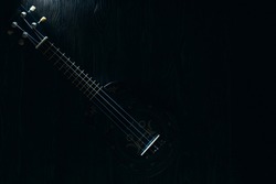Landscape in dark colors: a guitar with white strings on a dark wooden background, the neck in focus
