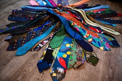 A bundle of colorful, oldfashioned business ties is lieing on a wooden floor.