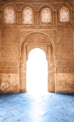 Sunshine through door to Granada palace. Sunlight on blue floor. Stone wall and windows in arabesque design. Ornate pattern of building in arabic style. Famous tourist destination in Spain, Europe.