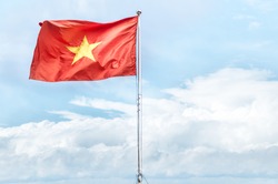 Metal pole with waving banner. Red flag with yellow star, blue sky with clouds in background. Rippled texture. National flag of Vietnam. Popular country for tourism. Famous tourist destination.