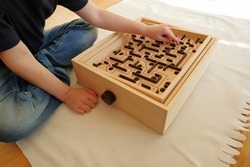 Sitting kid playing with a labyrinth maze game. Wooden toy, old style with a metal ball. No face. Stockholm, Sweden.