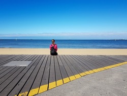 lonely woman with backpack sitting on beach pier with ocean view, time to think, enjoy the nature, being alone, meditation 