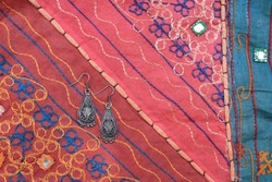 Indian silver earrings on the background of a traditional patchwork carpet. Indian background