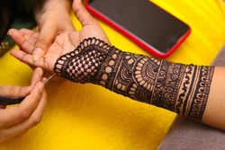 An Artist performing mehandi design on female hand close up image
