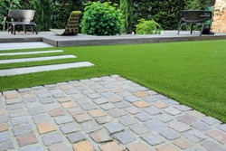Modern garden design and terrace construction with a material mix of cobble paving stones and concrete paving slab and artificial lawn and wood