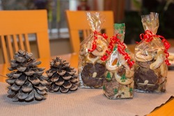 Seasonal homemade advent or christmas cookies in transparent bags gift wrapped with curled red ribbon placed on a table which is decorated with fir cones, bokeh lights, blurred background