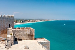View of the beach at Valencia and the castle of Peniscola. Spain. Beautiful coastline with beaches, hotels and turquoise sea. Part of the old fortress. Clear sunny day, cloudless sky.