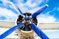 Old airplane engine with a propeller. Vintage fighter plane closeup by blue sky background.