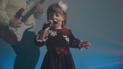 Little girl on stage in vintage dress, she sings into microphone and dances, her father plays an electric guitar. Color music is shining and smoke is billowing. Family time, creativity and hobbies