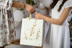 A gift from godparents for the first holy communion. A woman giving the girl a First Communion gift. First Communion gifts in decorative bags.