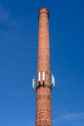 5G antennas on a brick pipe against a clear sky. Cellular and internet antennas on the brick pipe of the boiler room. The top of a chimney with a cell phone antenna. An old red brick factory chimney.