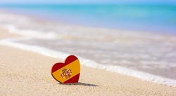 Flag of Spain in the shape of a heart on a sandy beach. The concept of the best vacation in Spain