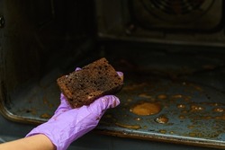 A woman's hand shows a very dirty sponge after cleaning the oven. Detergent efficiency concept. Selective focus on the sponge.